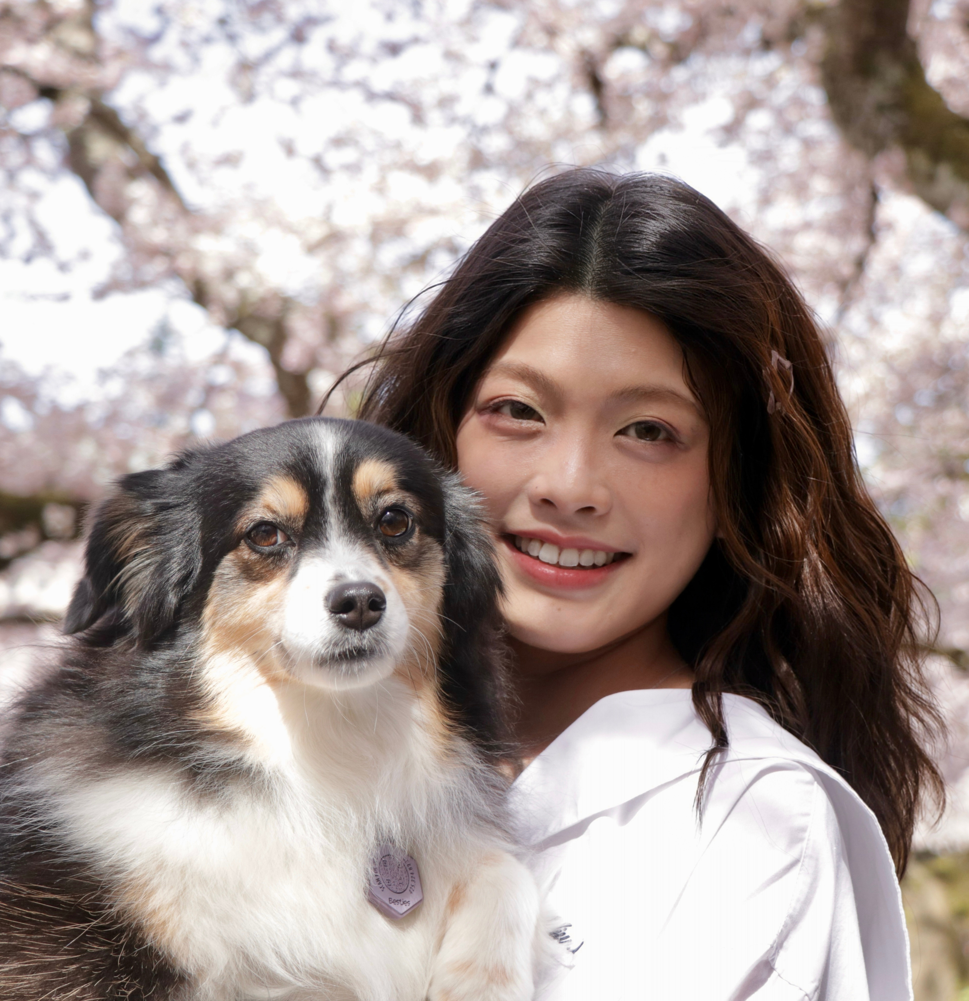 Angela smiling outdoors with her dog under cherry blossoms